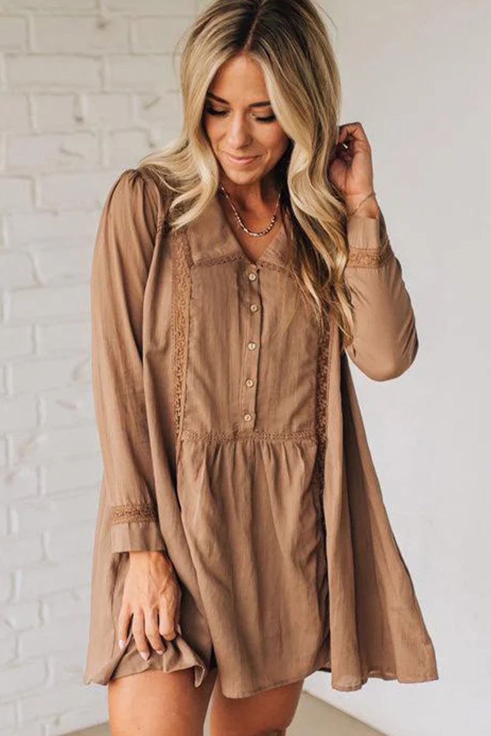 Woman wearing a loose-fitting tan button-front dress with lace trim details, long sleeves