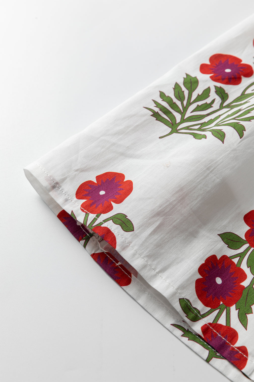 White fabric with red and purple floral print and green leaves, close-up view