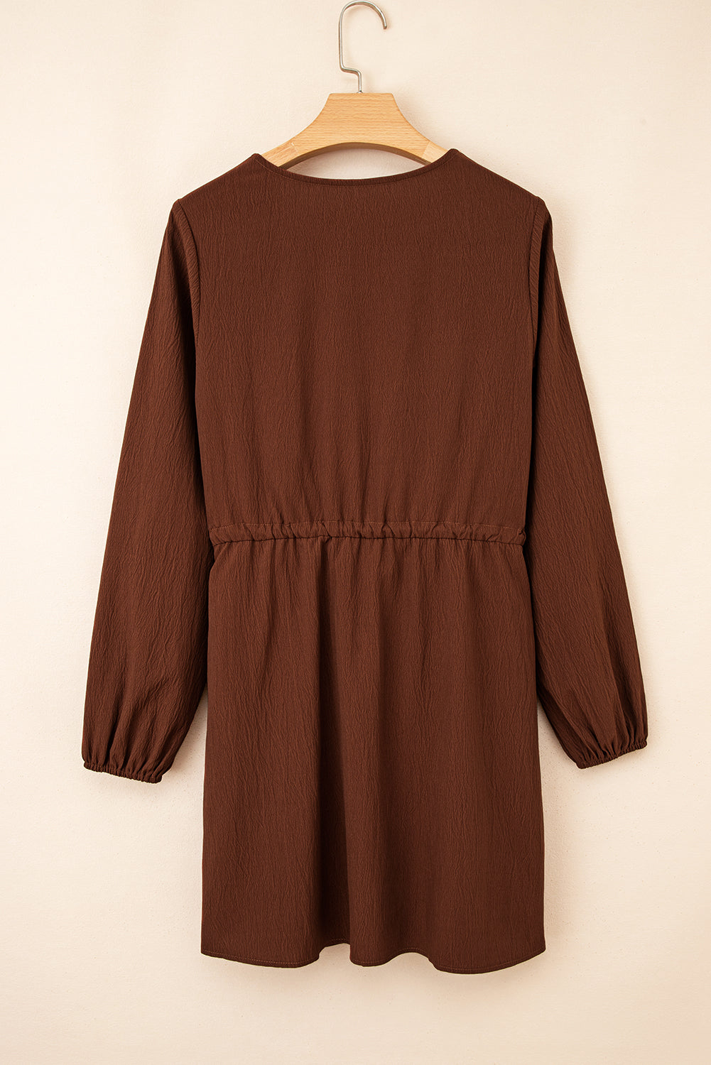 Back view of a brown long sleeve mini dress with elastic waist, hanging on wooden hanger