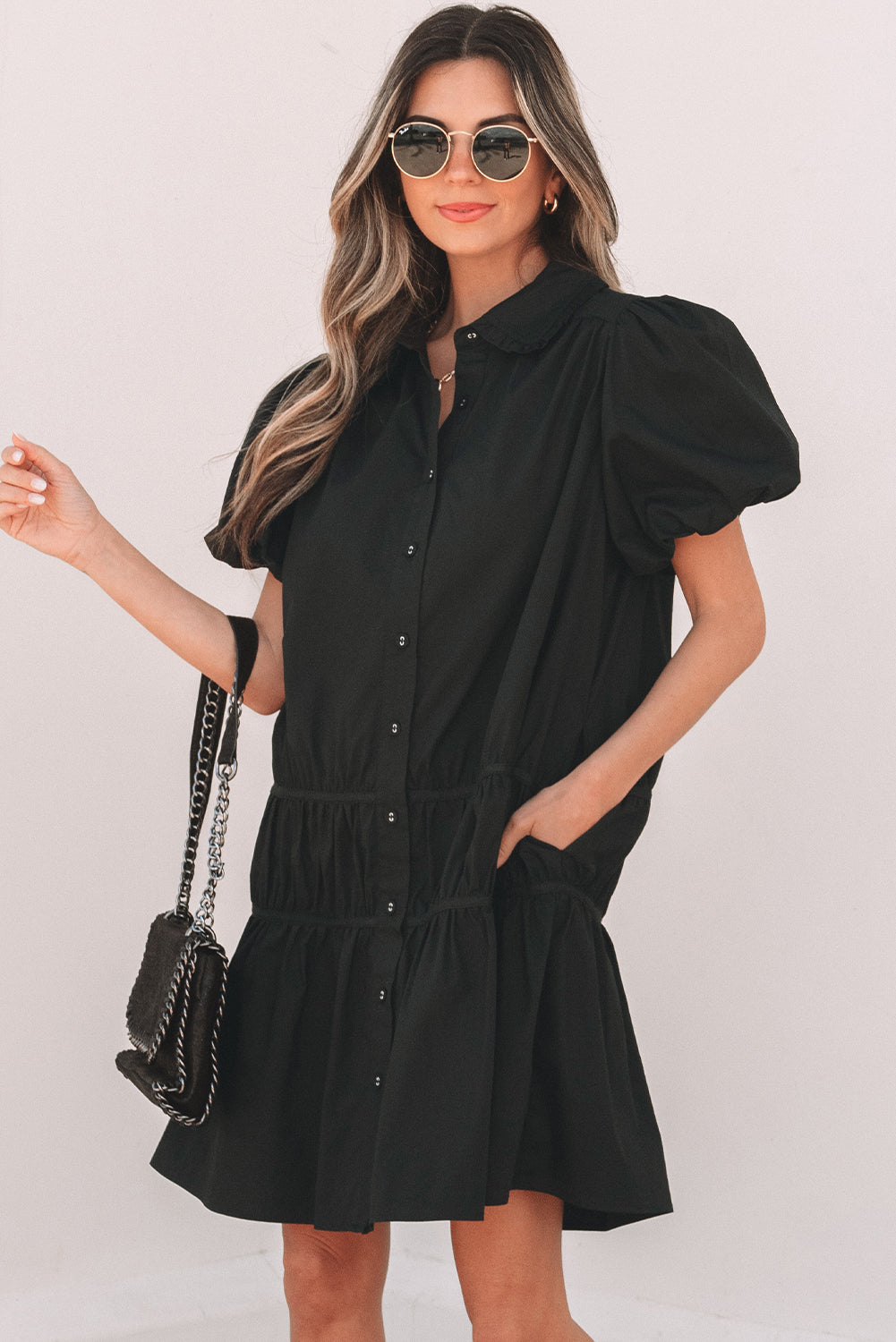 Woman in a black puff sleeve button-up dress with sunglasses and a chain shoulder bag