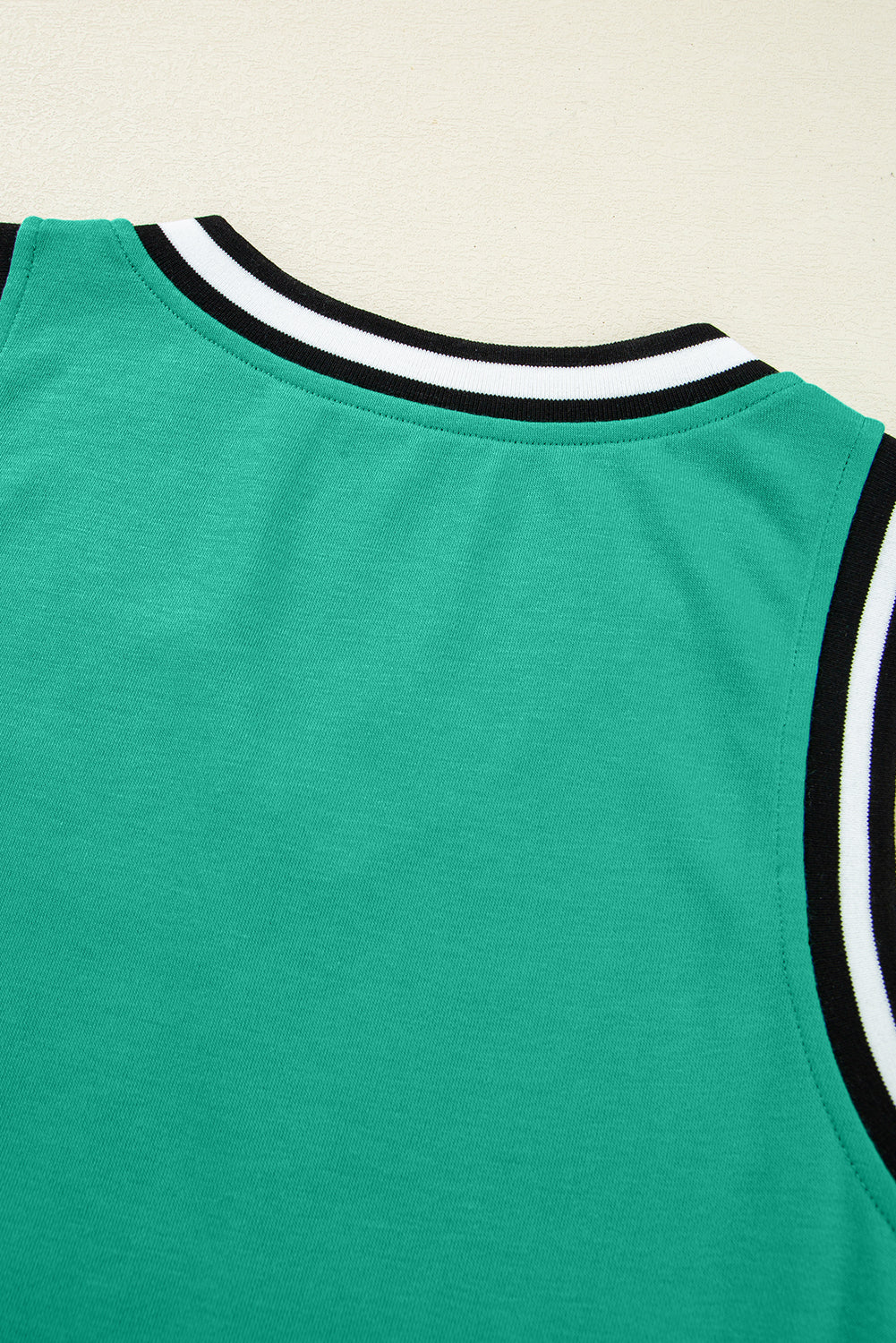 Close-up of a green sleeveless top with black and white striped collar and armholes