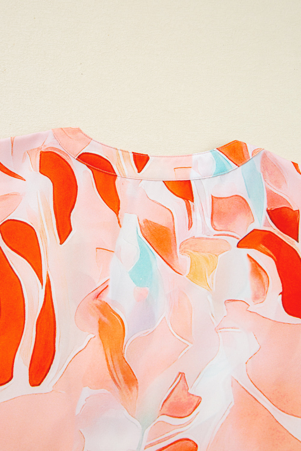 Close-up of a blouse with abstract orange, pink, and light blue floral print