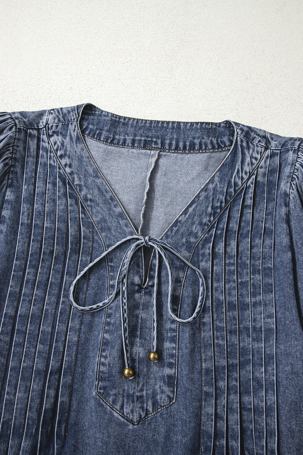 Close-up of denim blouse with V-neck, pleated details, and tie string with metal beads