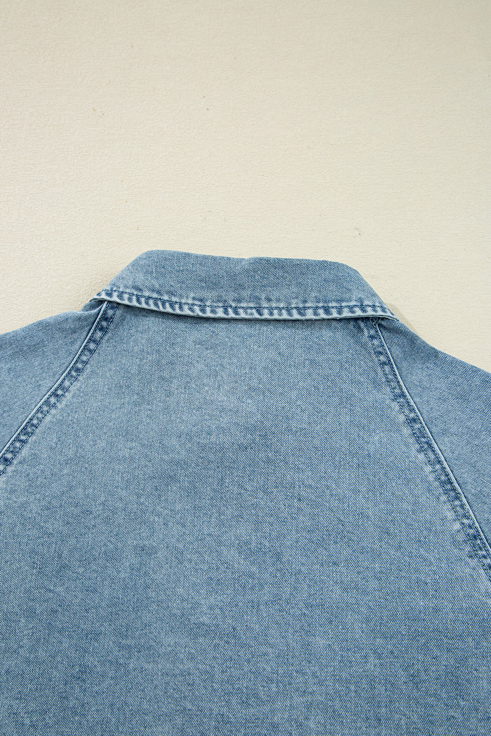Close-up of light blue denim jacket collar and back with visible stitching