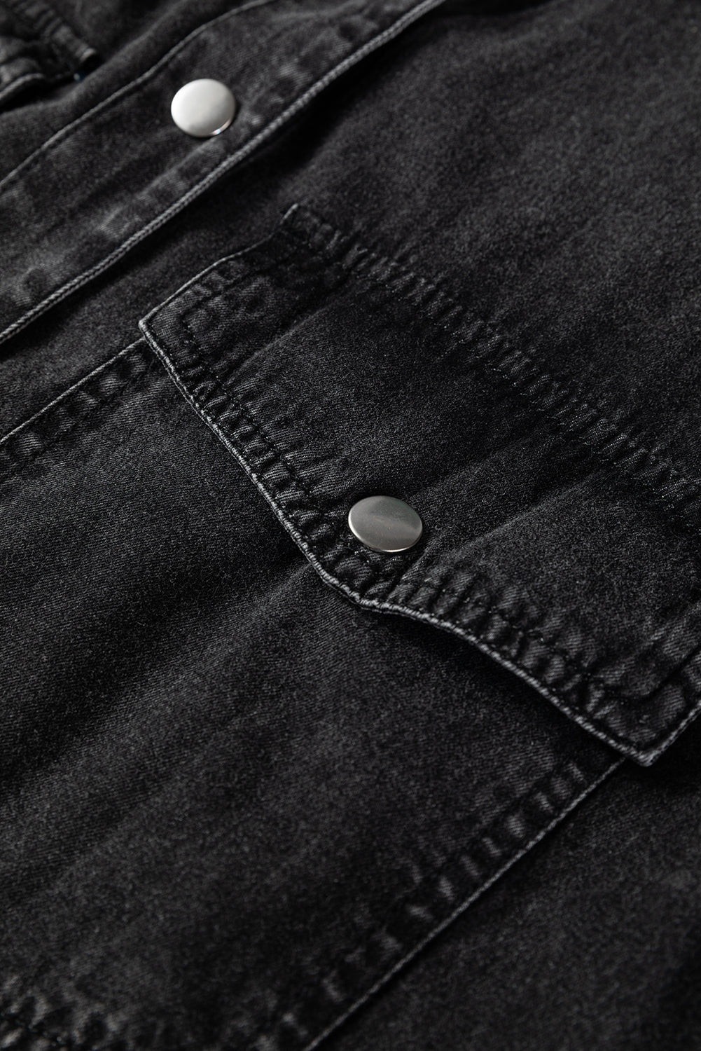 Close-up of black denim jacket pocket with silver button detail