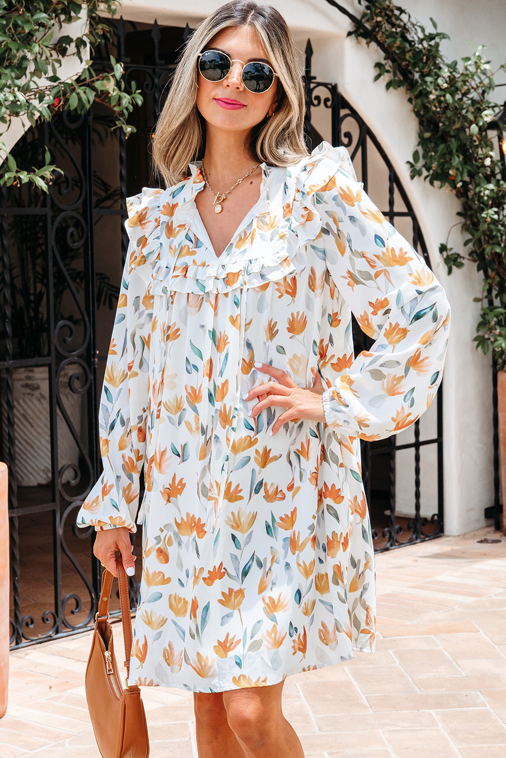 Woman wearing a white floral long sleeve dress with ruffle details, holding a brown handbag