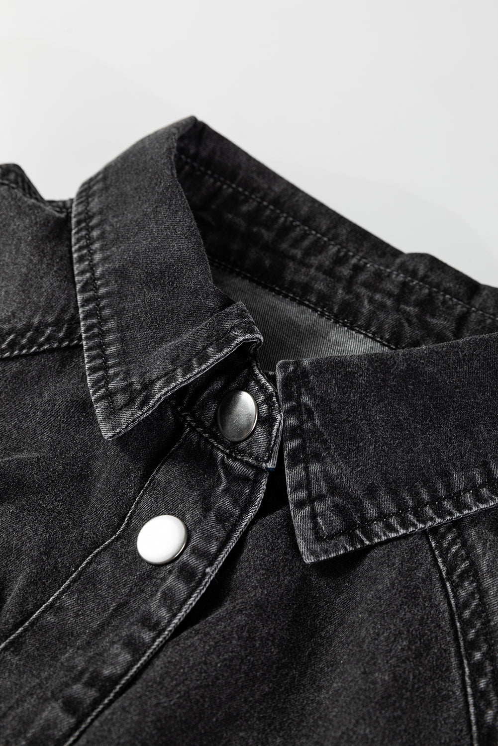 Close-up of black denim jacket collar with metal snap buttons, casual fashion