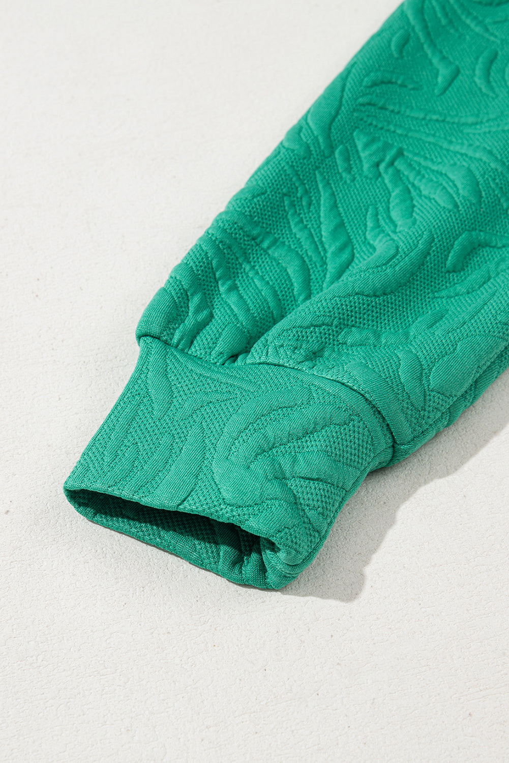 Close-up of textured green sleeve with ribbed cuff on light background