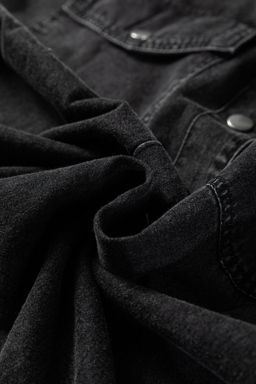 Close-up of soft black denim fabric with metal buttons and a chest pocket