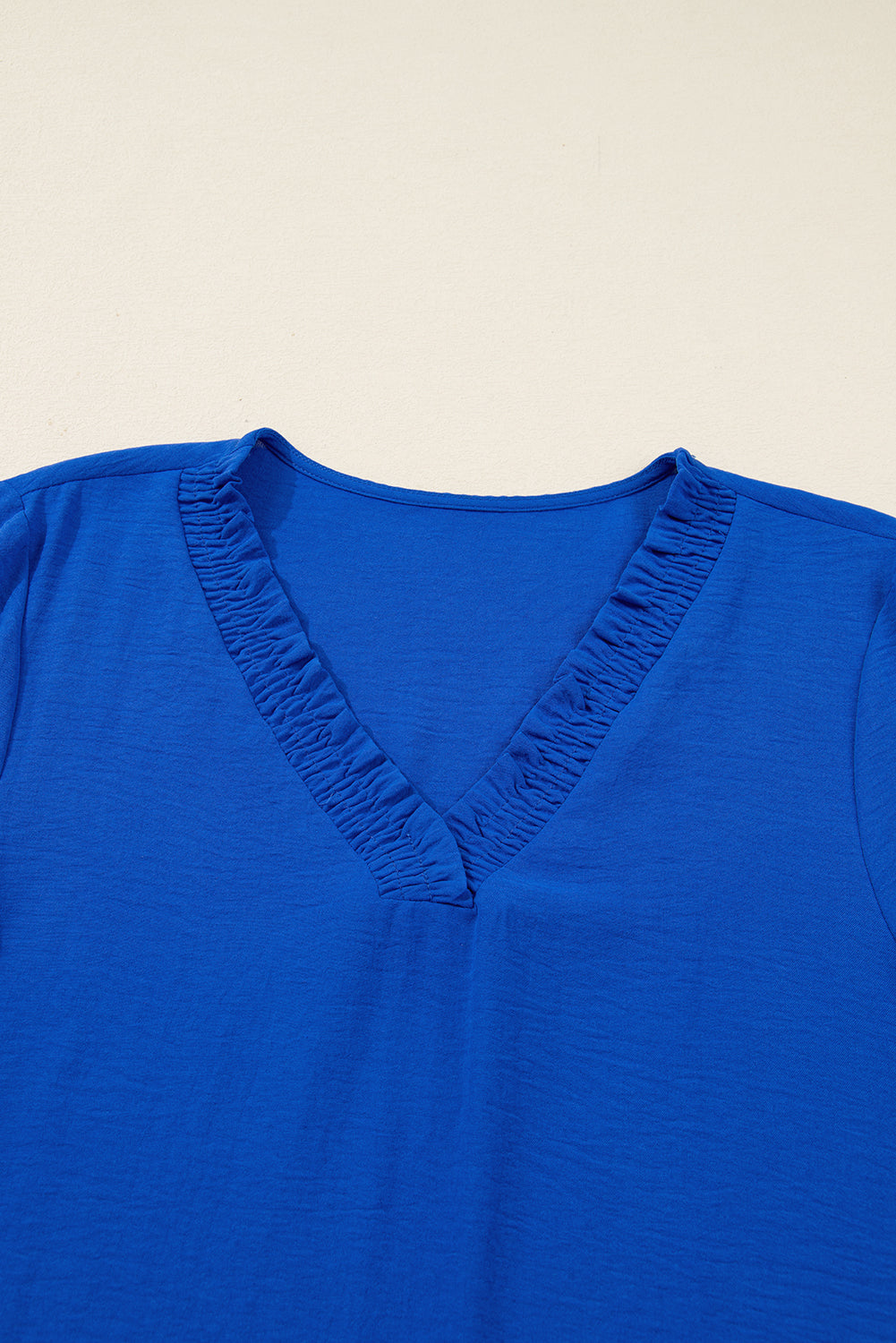 Bright blue women's top with V-neck and ruched neckline detail on cream background