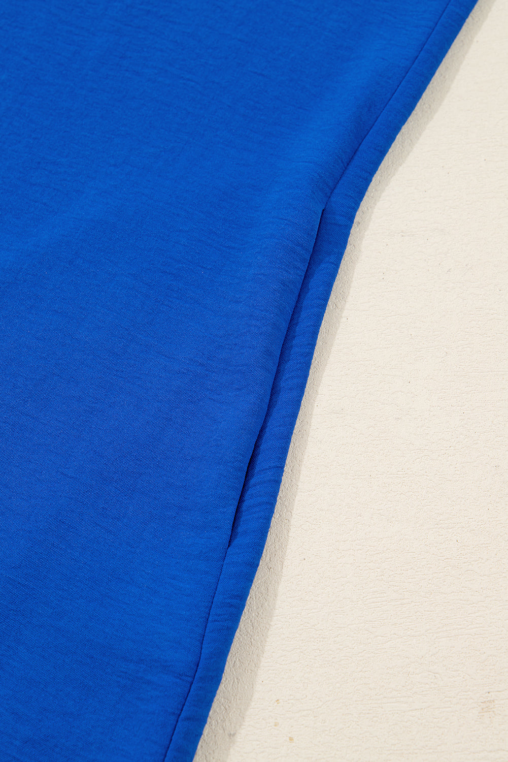 Close-up of bright blue fabric pants with a side seam detail on a light background