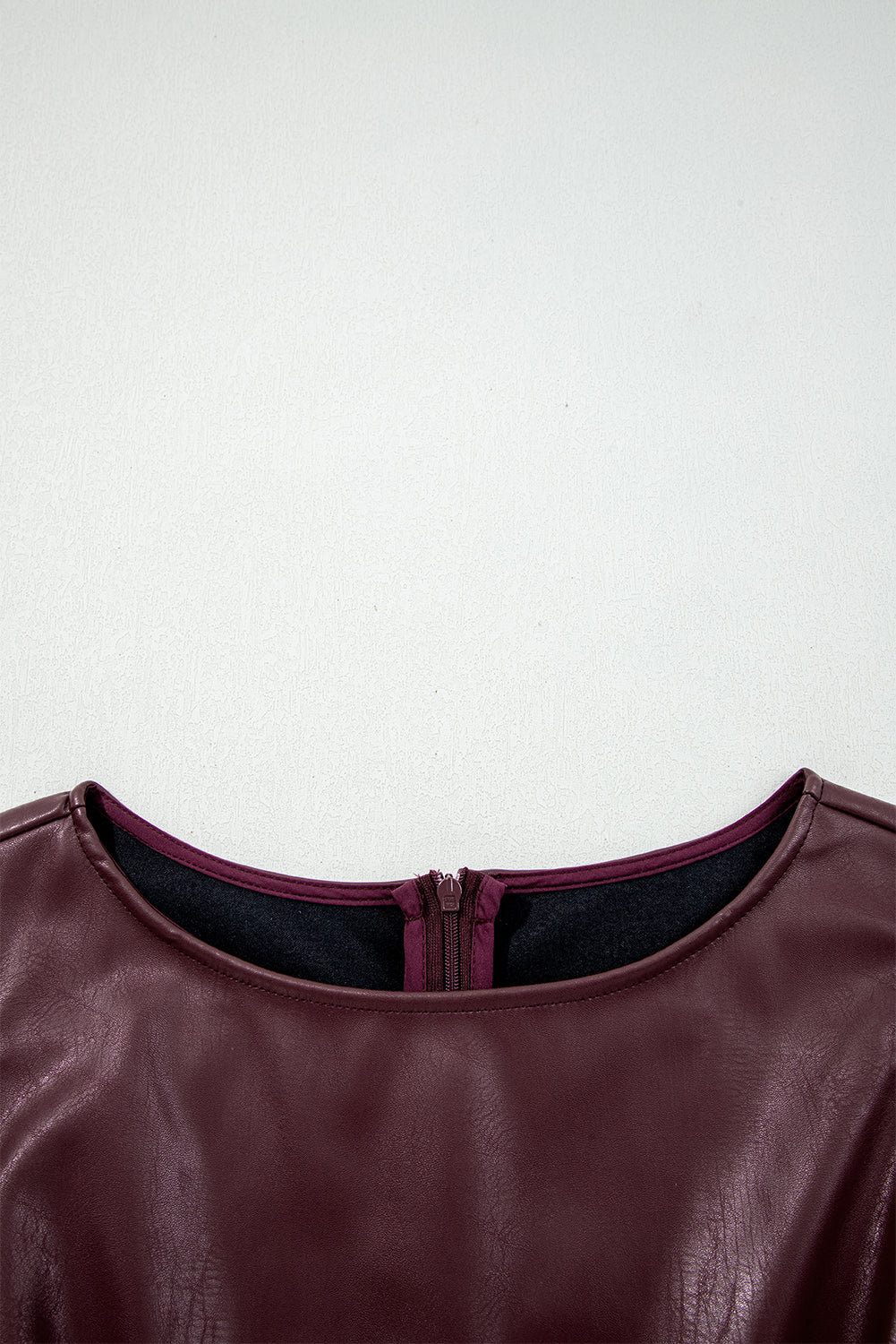 Close-up of a burgundy faux leather dress with a back zipper and round neckline