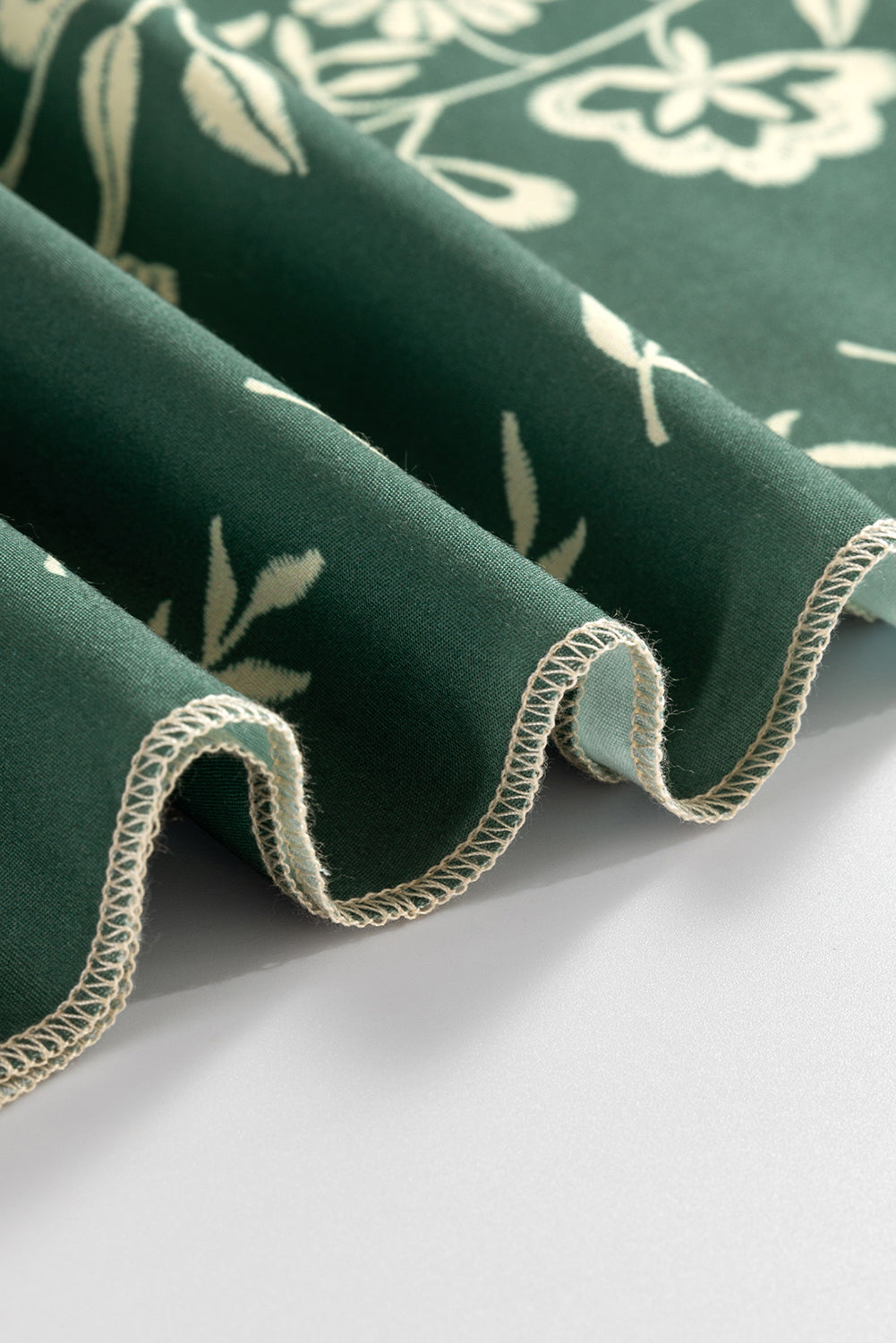 Close-up of green floral fabric with white flower pattern and stitched edge