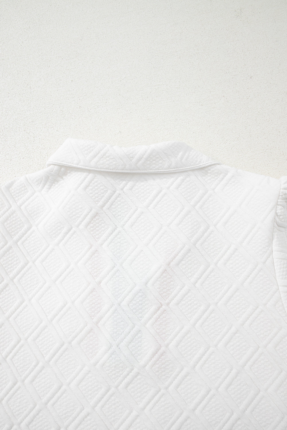 White textured diamond pattern fabric with collar detail, close-up view
