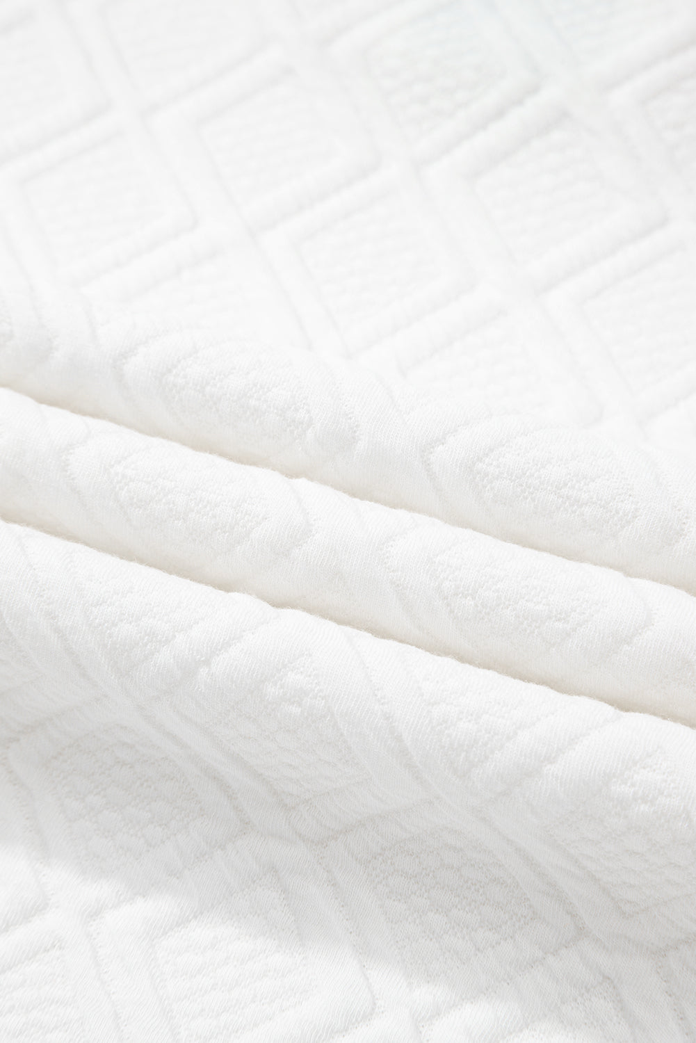 Soft white textured fabric with geometric diamond pattern, close-up textile detail