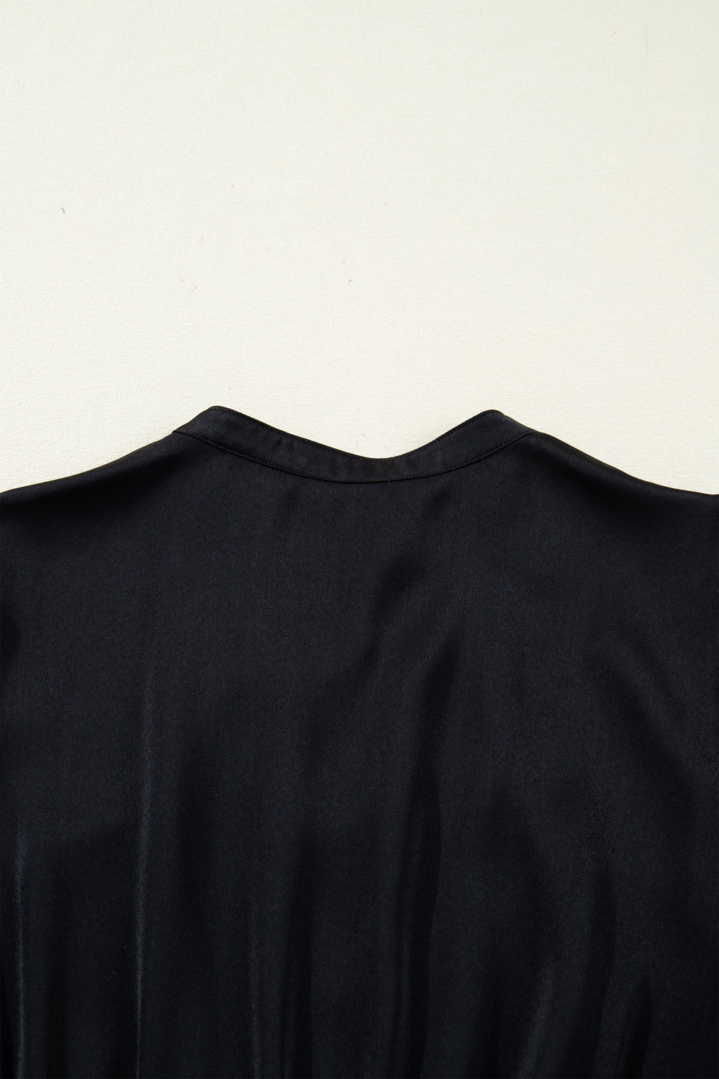 Close-up of black satin blouse back with V-neck on light background