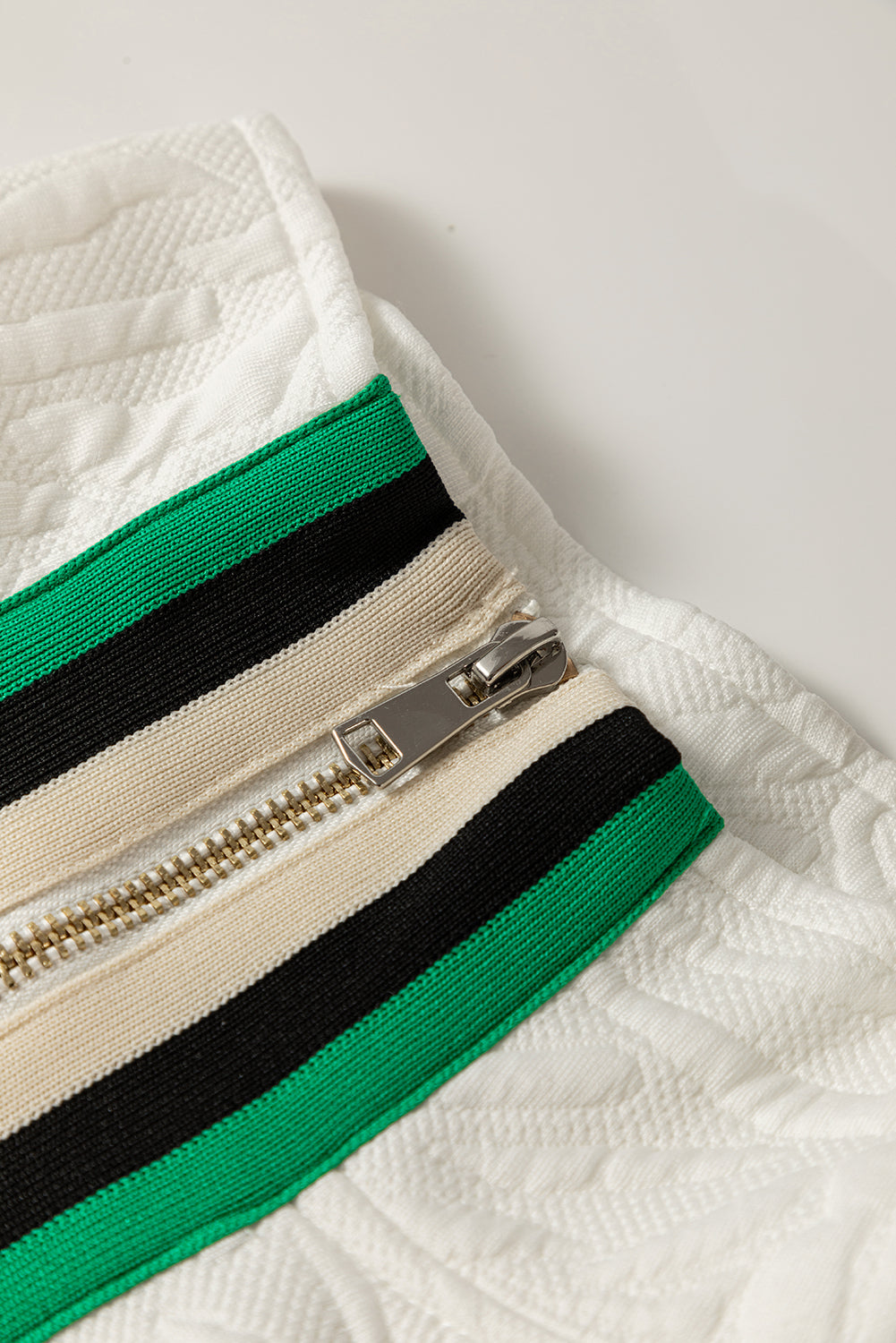Close-up of white textured fabric with silver zipper and green, black, cream stripes