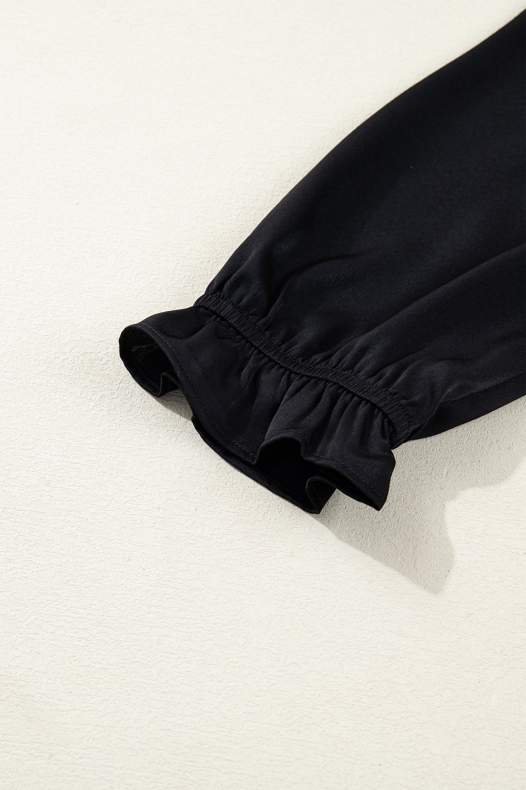 Black long sleeve with ruffled elastic cuff detail on light textured background