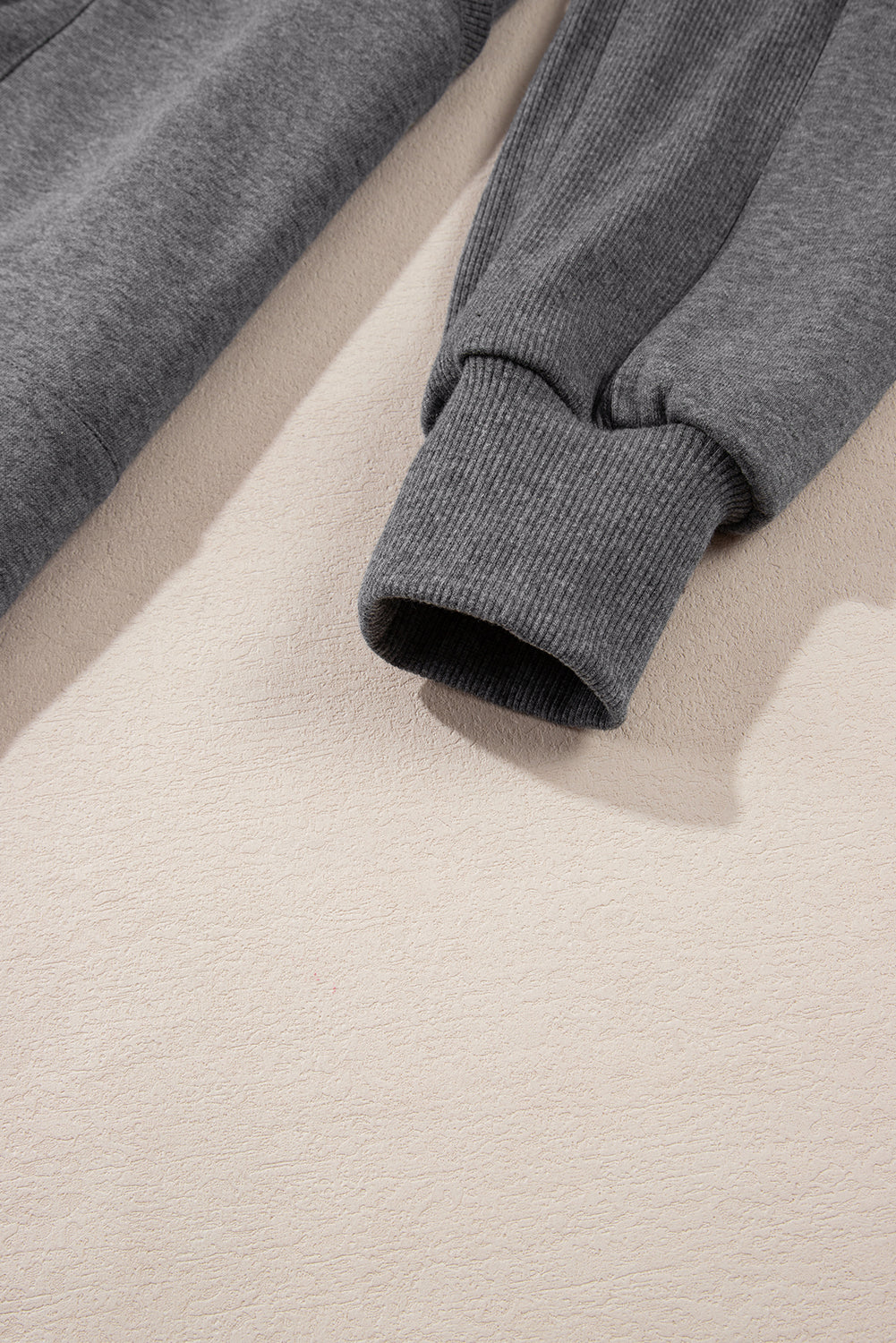 Close-up of grey sweatshirt sleeves with ribbed cuffs on beige background