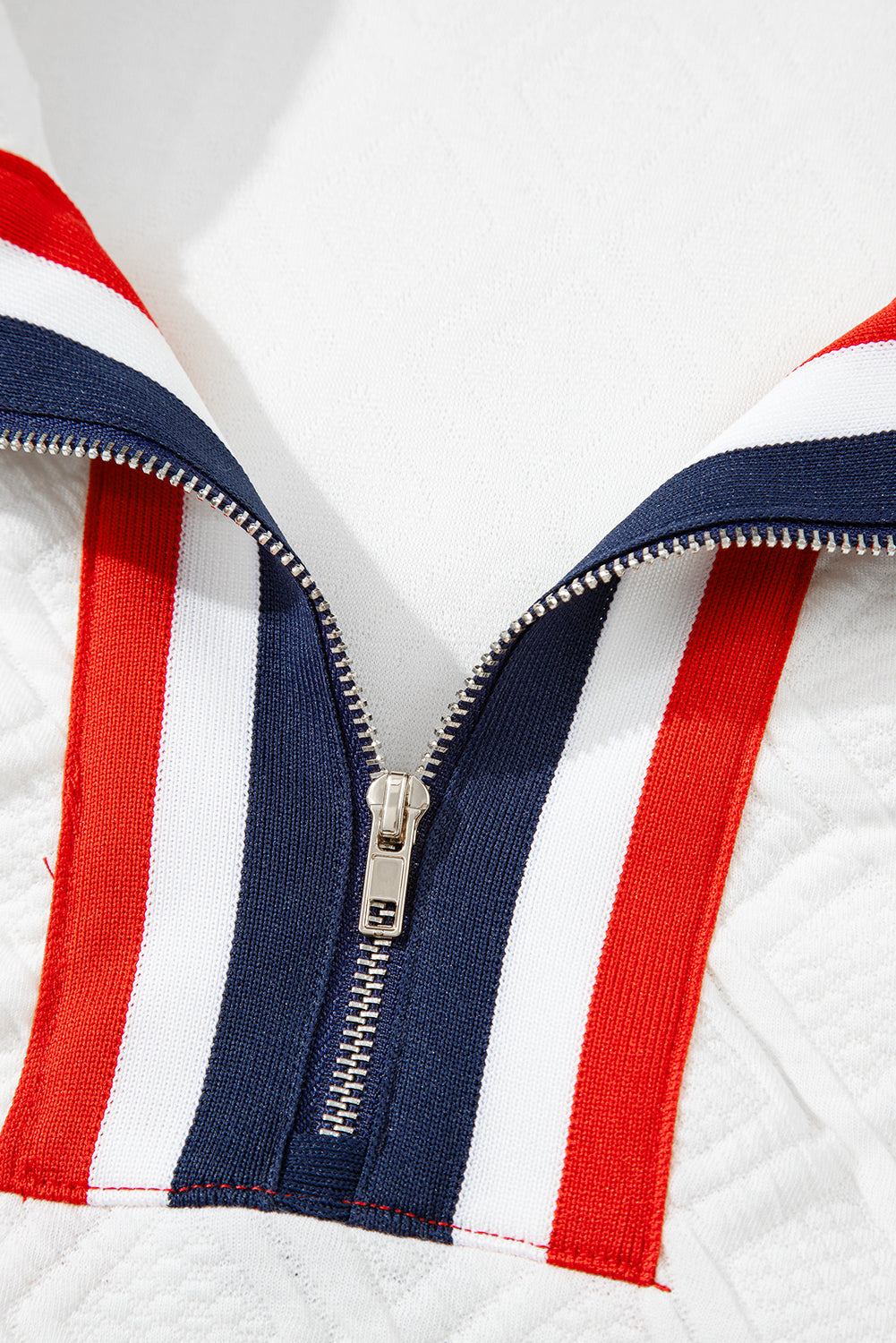 Close-up of a metallic zipper on white fabric with red, white, and blue striped trim