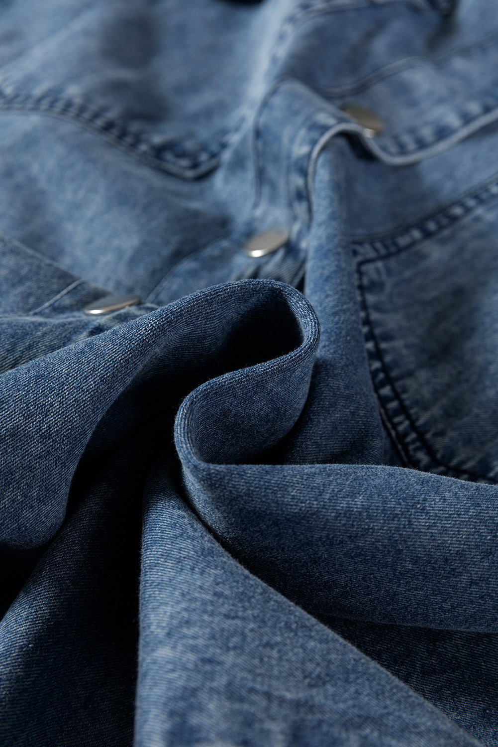 Close-up of blue denim fabric with metal buttons, showcasing texture and stitching