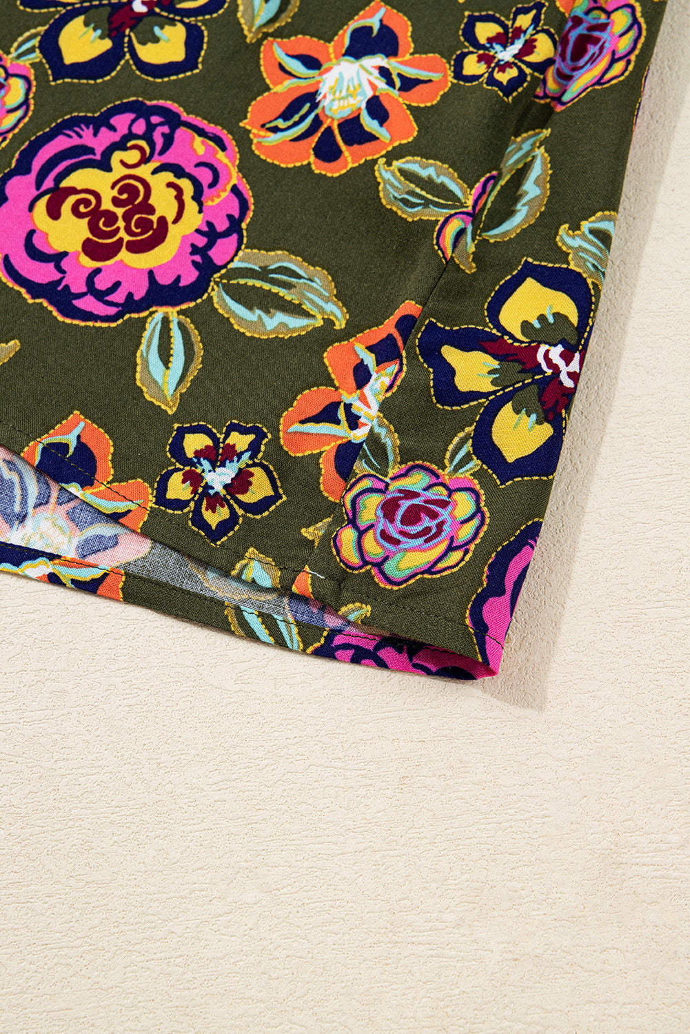 Green fabric with bright floral print in orange, pink, yellow and blue tones, close-up view