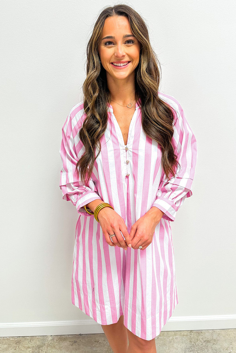 Woman wearing a pink and white striped button-down shirt dress, smiling indoors