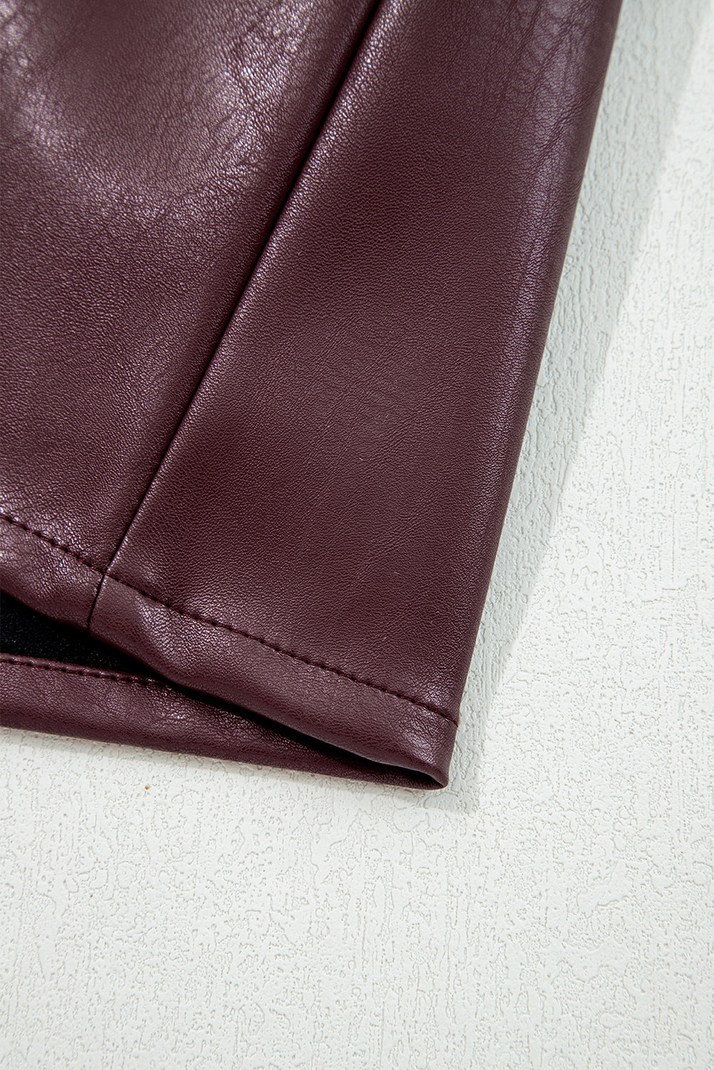 Close-up of maroon faux leather skirt hem with textured finish on light background