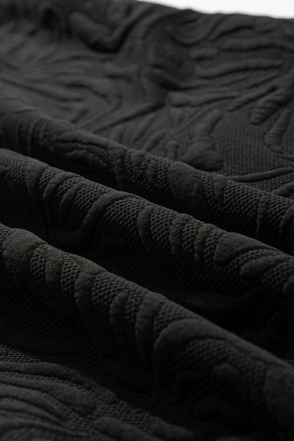 Close-up of black textured fabric with embossed floral pattern, soft textile material