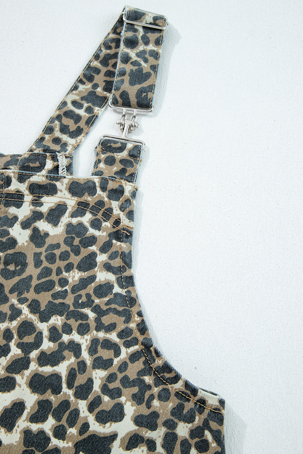 Close-up of leopard print overall strap with metal buckle on white background