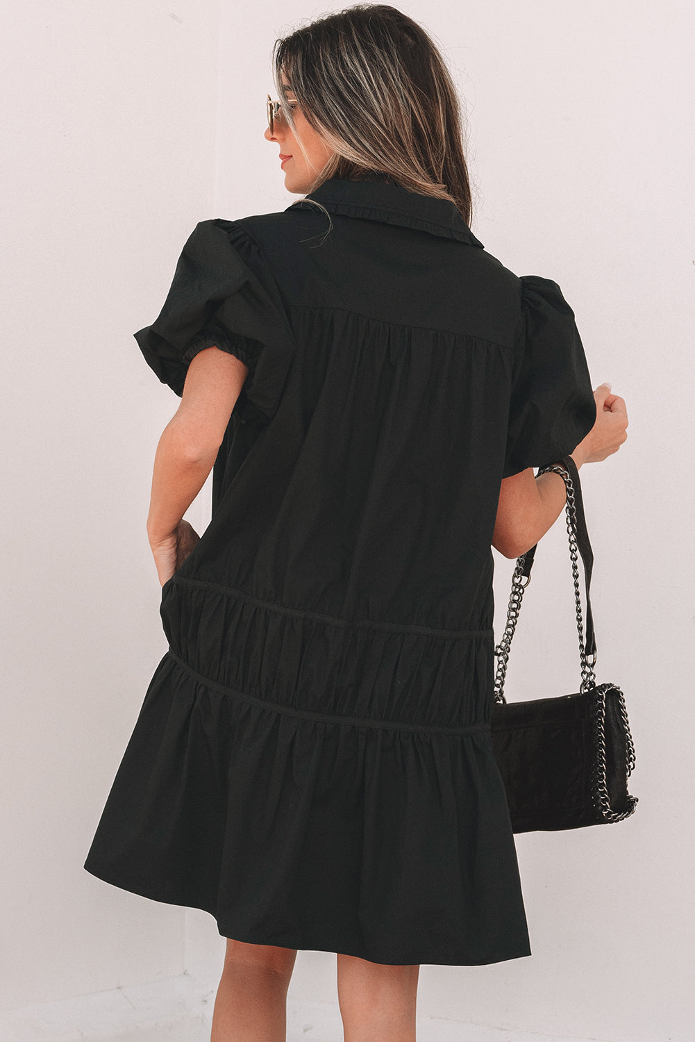 Woman in black puff sleeve dress with ruffled skirt holding a black chain shoulder bag