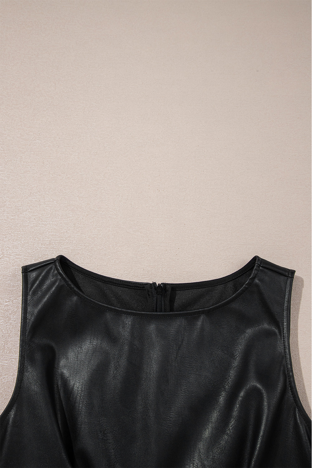 Black faux leather sleeveless dress with round neckline and back zipper on beige background