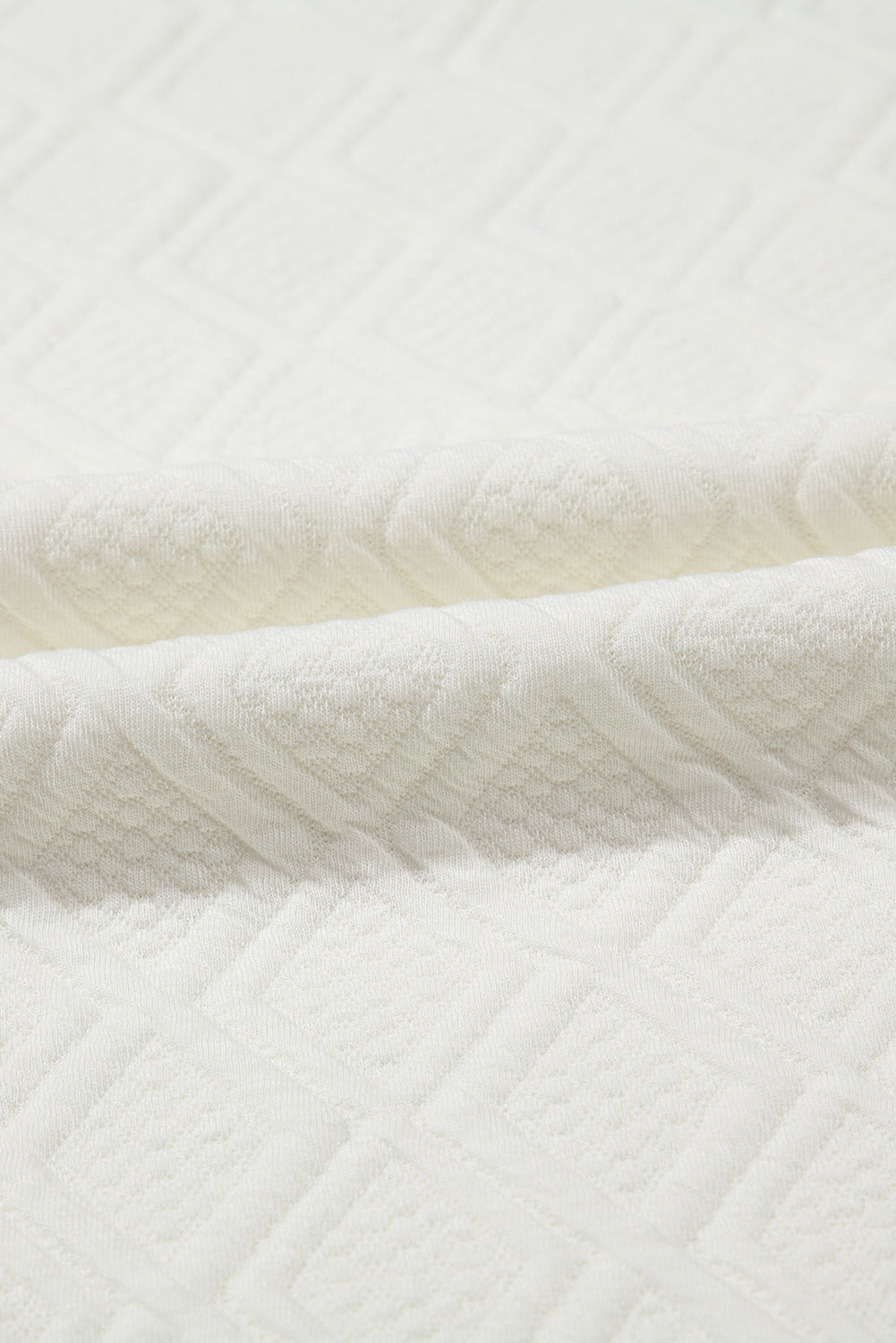 Close-up of soft white textured fabric with geometric diamond pattern, bedding textile