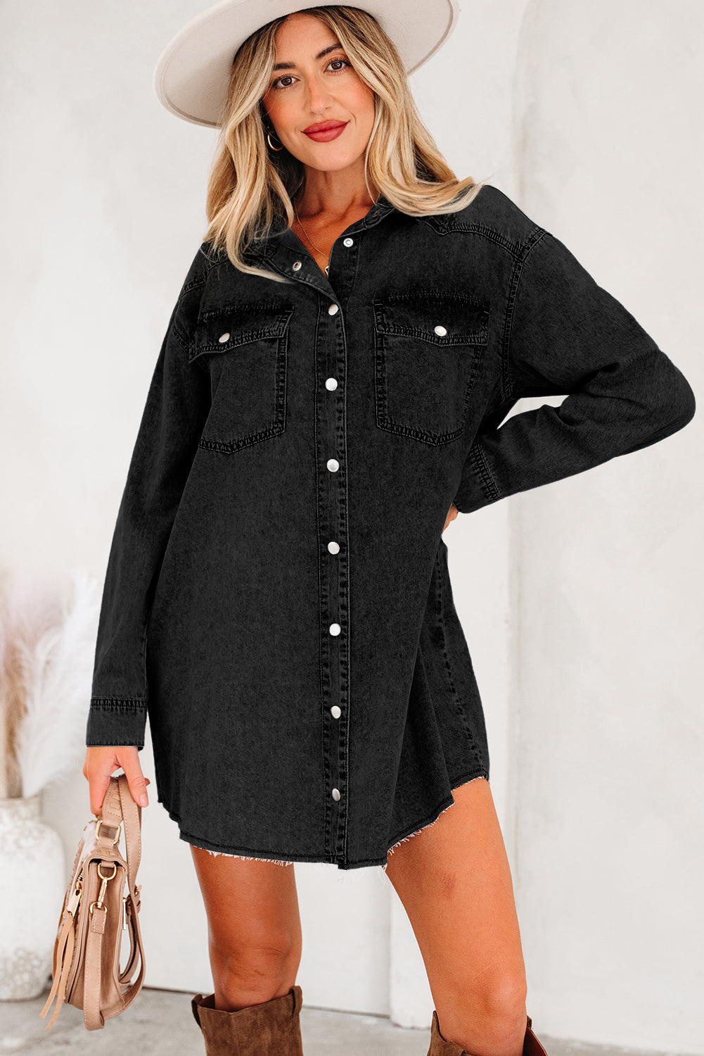 Woman in black denim shirt dress with button front, white hat, brown boots, holding handbag