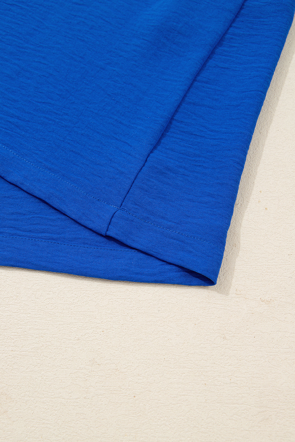 close-up of blue cotton t-shirt hem on beige textured surface