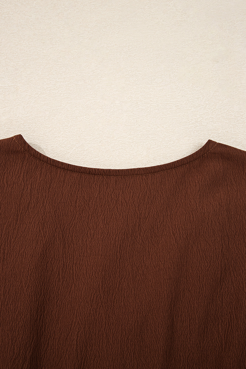 Close-up of brown textured blouse with round neckline on neutral background