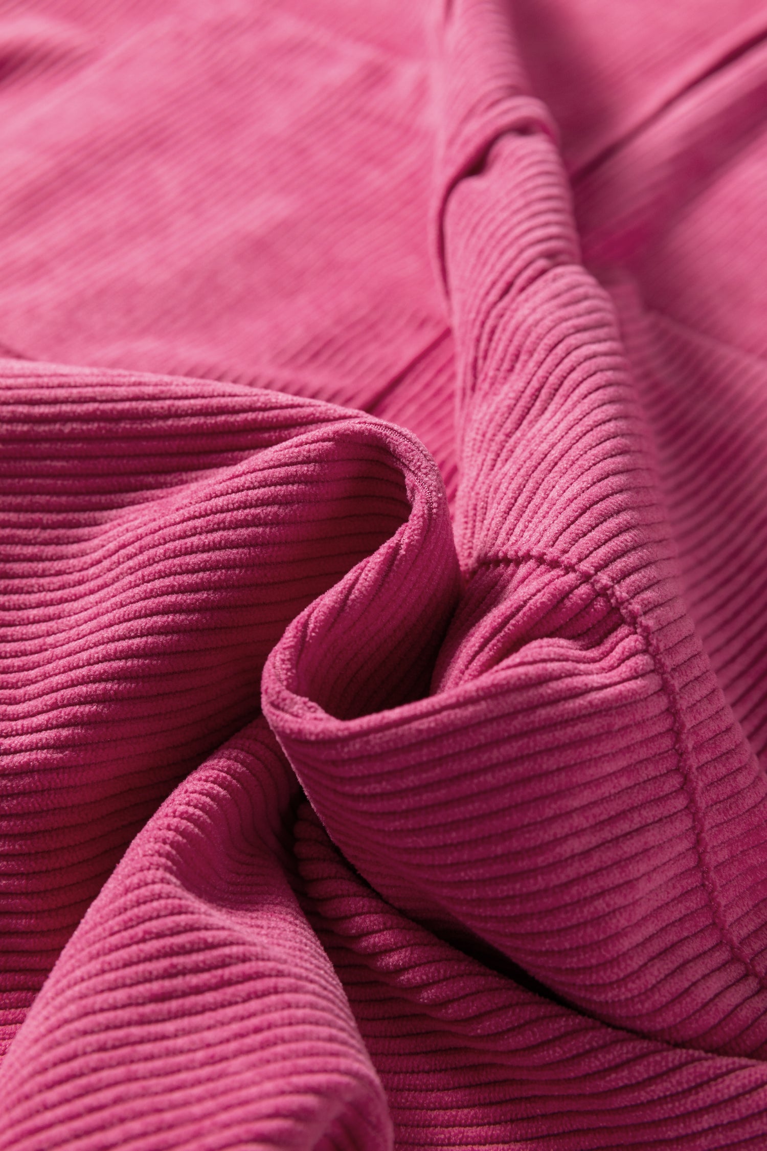 Close-up of pink ribbed corduroy fabric with soft, textured folds