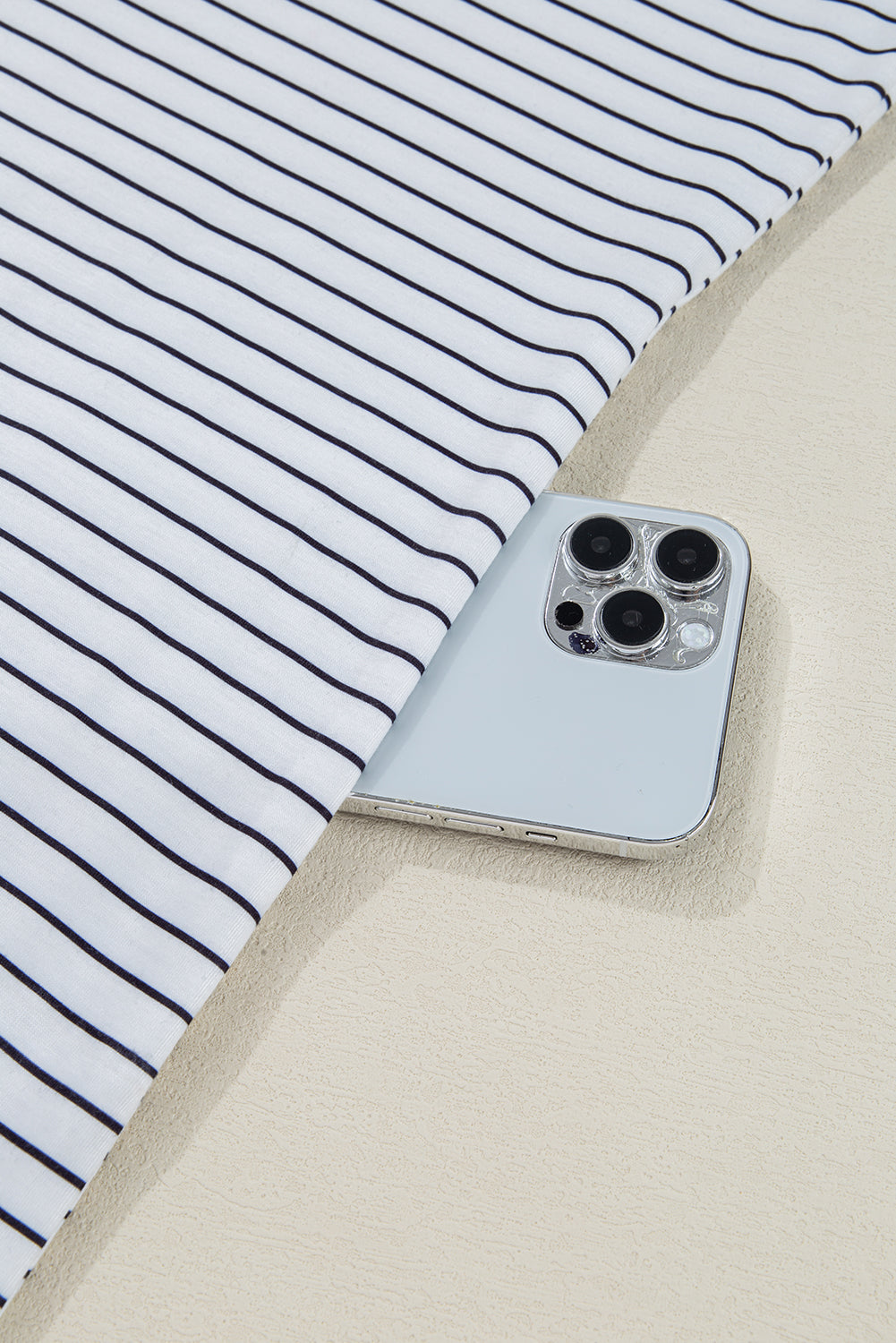 Smartphone partially covered by white fabric with black stripes on beige surface