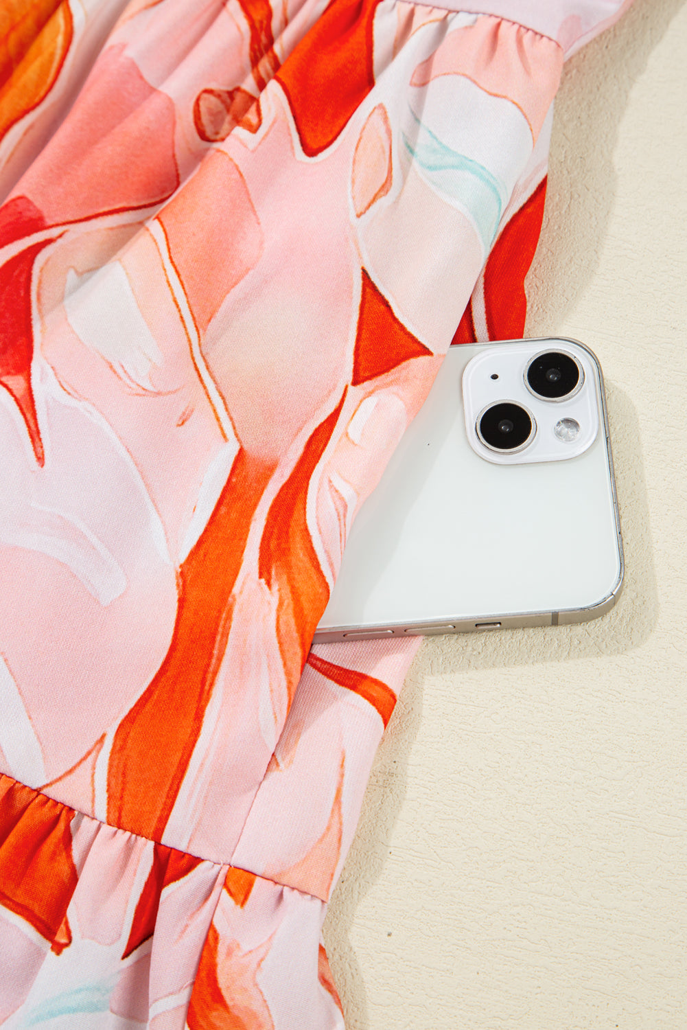 White smartphone in pocket of pink and orange patterned dress on beige surface