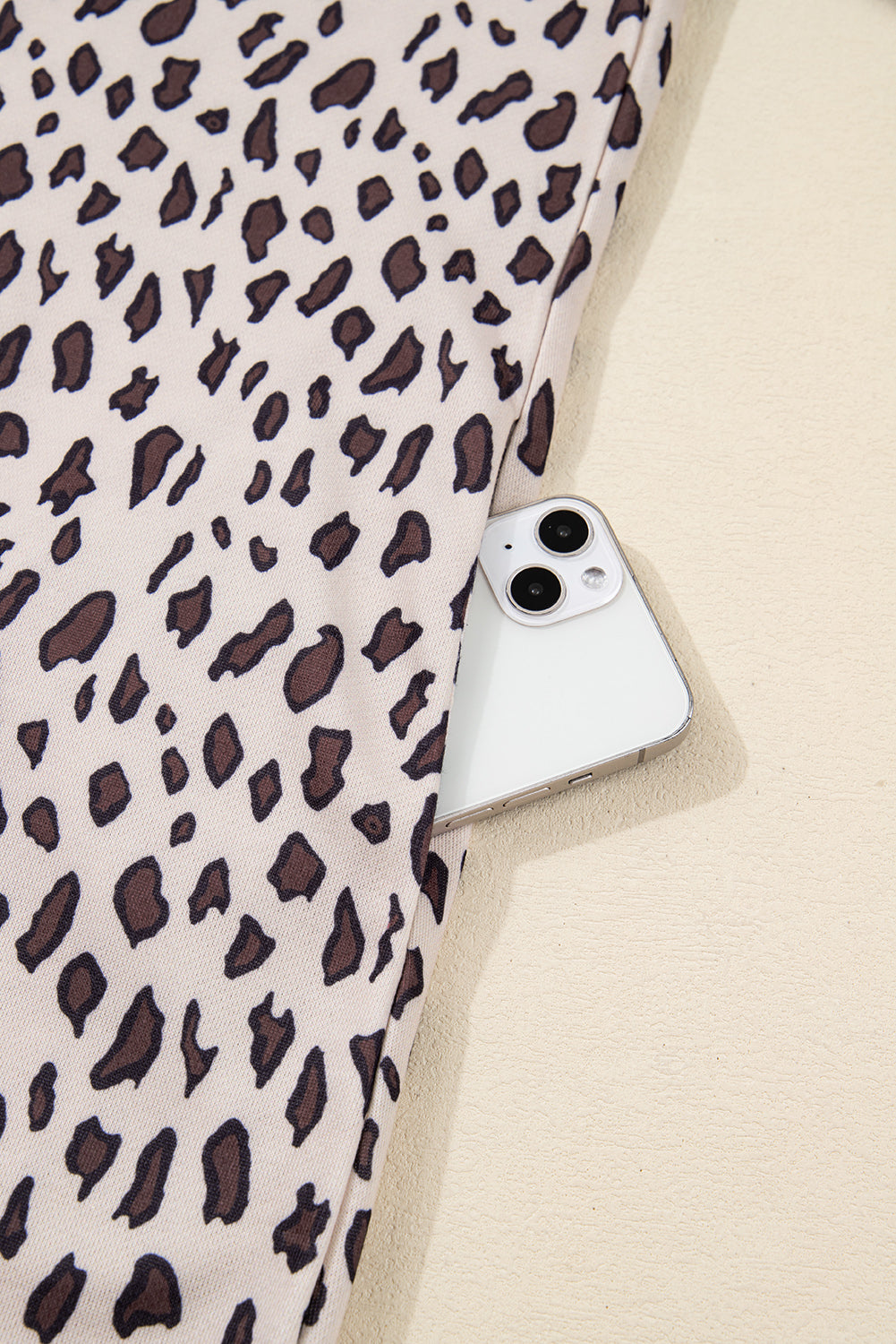 Leopard print fabric pocket with white smartphone partially inside on beige background