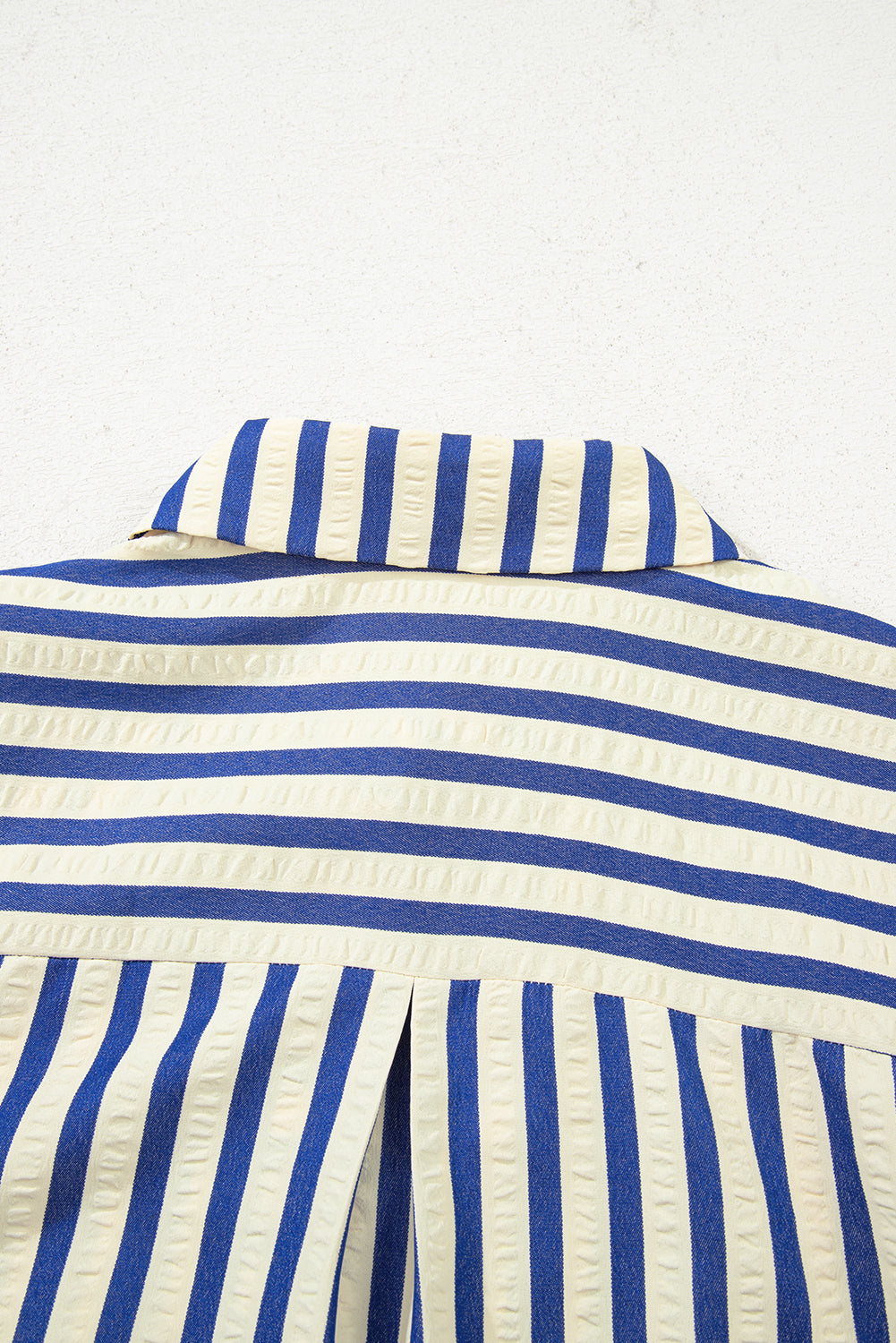 Close-up of a blue and white striped shirt collar and back with textured fabric.