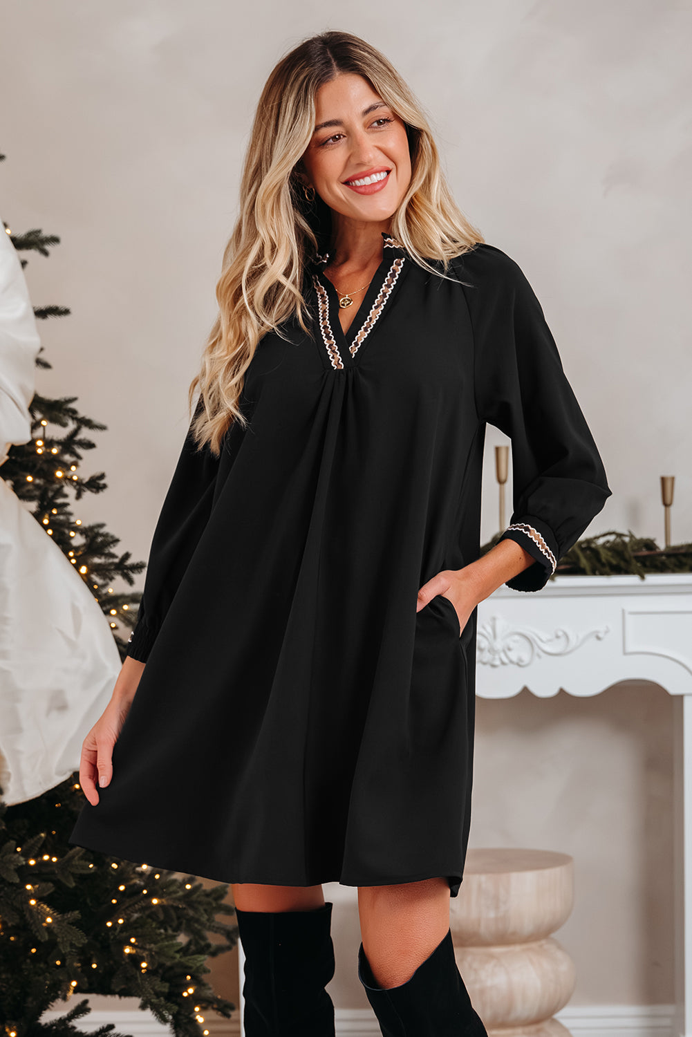 Woman in black long sleeve dress with lace trim, standing by Christmas tree