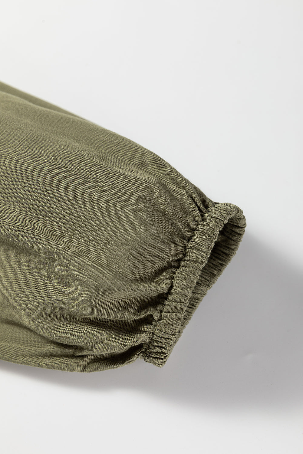 Close-up of olive green sleeve with elastic cuff, lightweight fabric texture