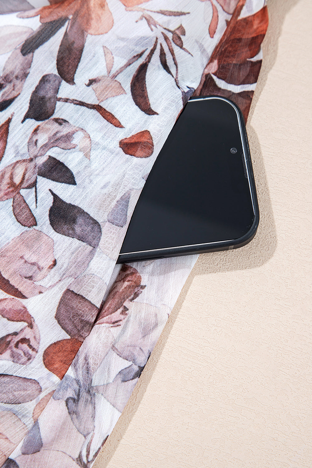 Smartphone tucked into floral print sheer fabric pocket on a beige surface