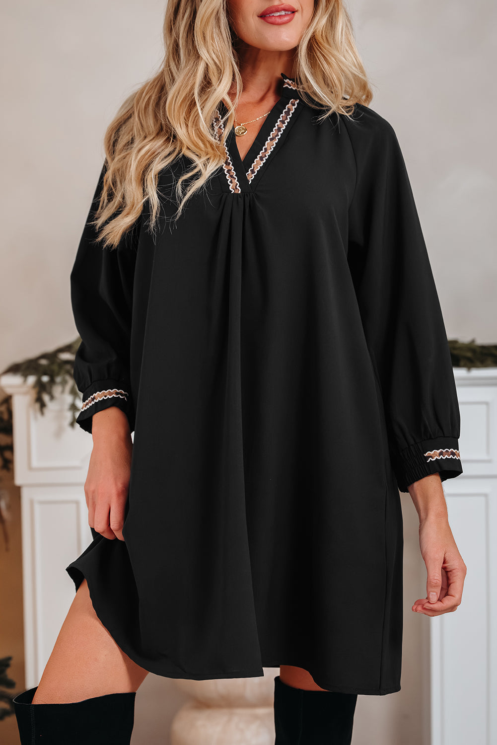 Woman wearing a black long sleeve dress with embroidered trim and knee-high boots