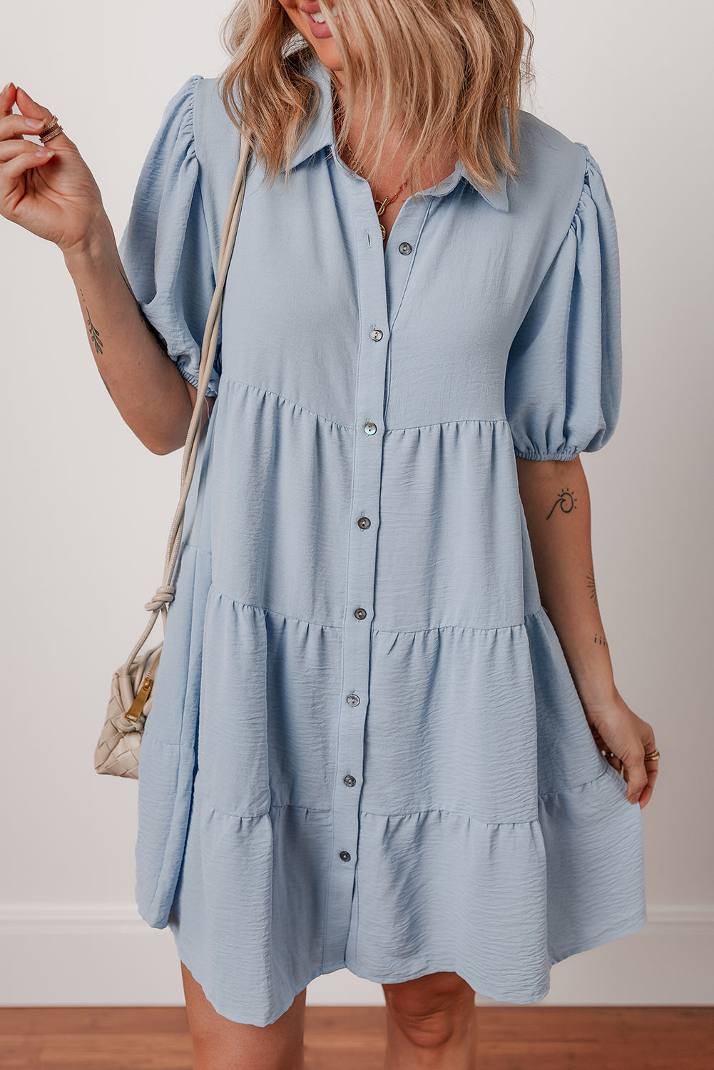 Woman wearing light blue button-up short dress with puff sleeves, casual summer style