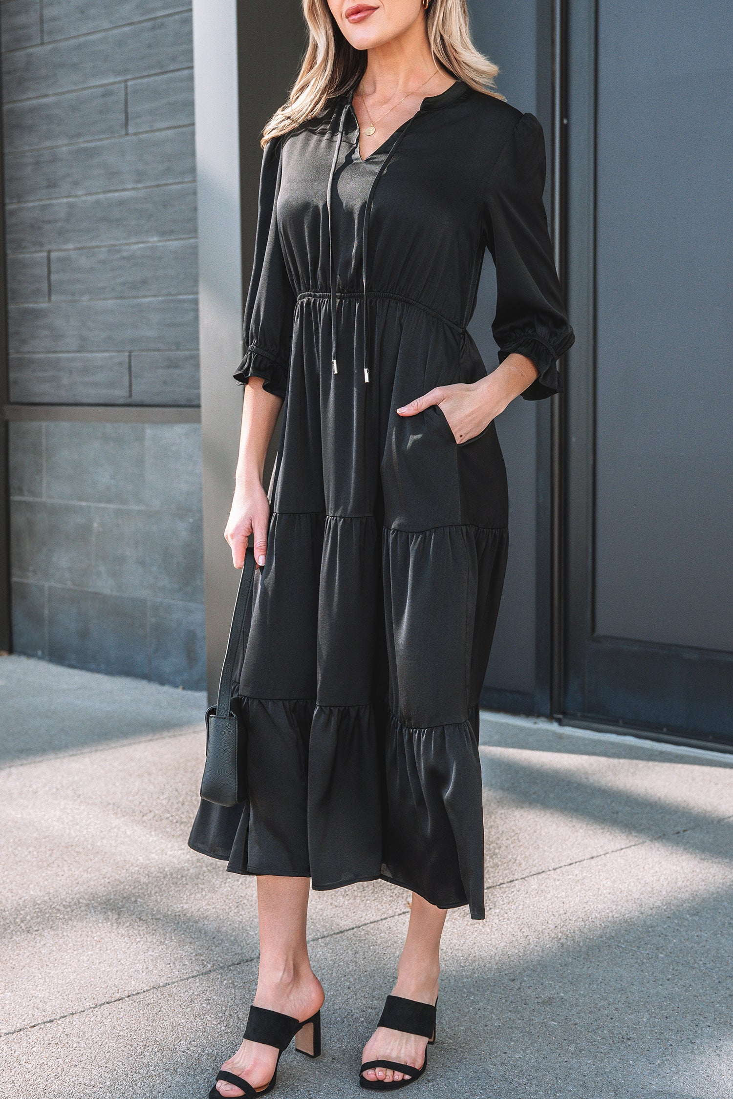 Woman wearing a black tiered midi dress with three-quarter sleeves and heeled sandals outdoors