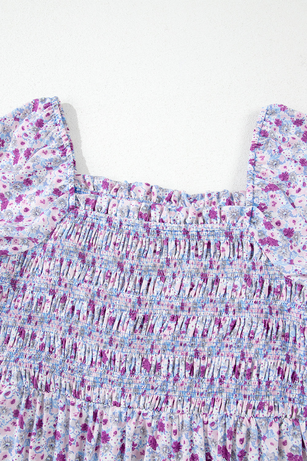 Close-up of smocked floral dress bodice with purple and blue flowers, ruffled sleeves