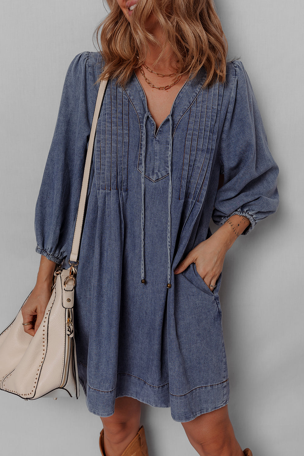 Woman wearing a denim dress with puff sleeves, accessorized with a beige shoulder bag