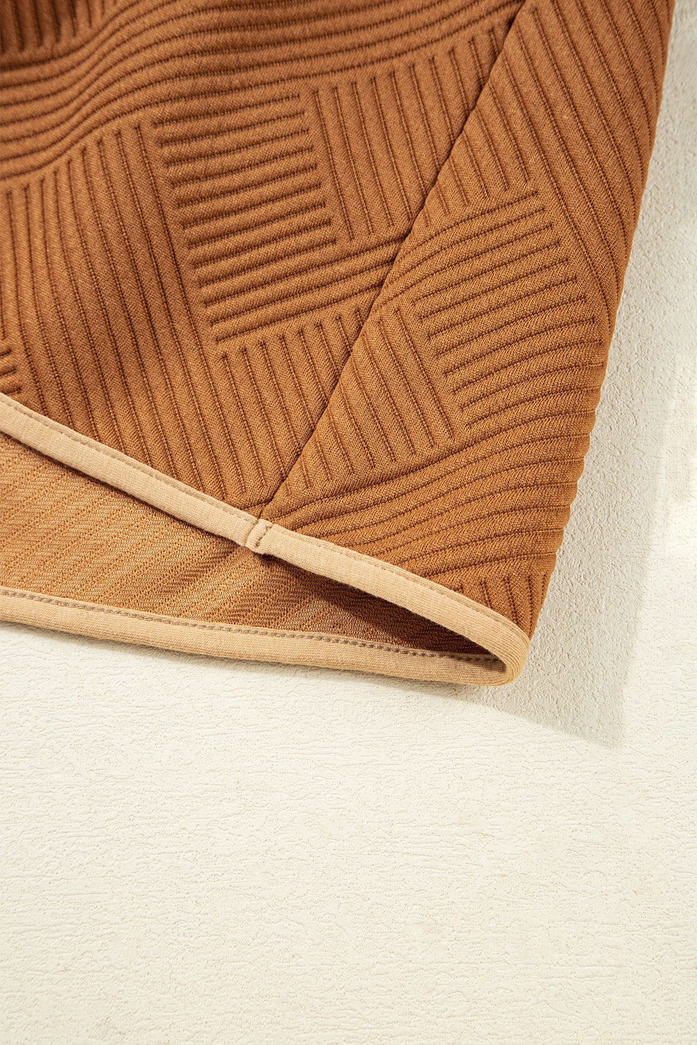 Close-up of brown ribbed textured fabric with geometric pattern and beige hem